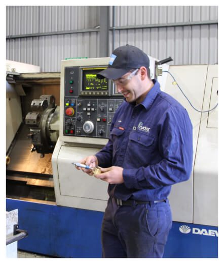 A man in front of a big machine smiling while looking at his phone - Ryder Machining Specialists
